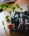 Coffee setup with a cup, carafe, and coffee bag on a wooden table.