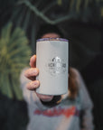 A person holds a gray travel mug with "Anchorhead Coffee Co." logo in focus. The background features blurred tropical leaves, creating a calm, inviting tone.